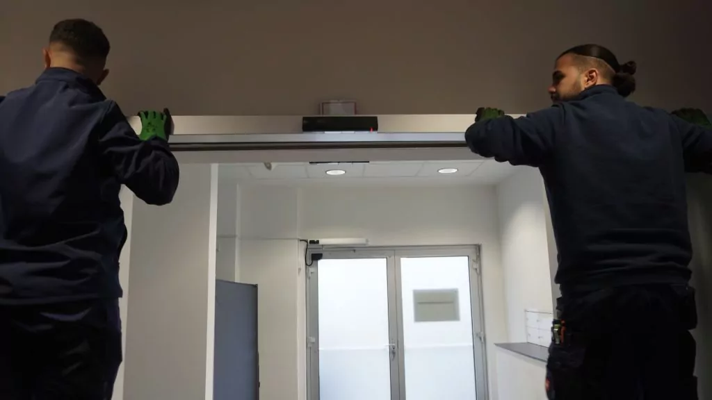 Zwei ATH-Techniker prüfen den oberen Bereich eines automatischen Türsystems.
