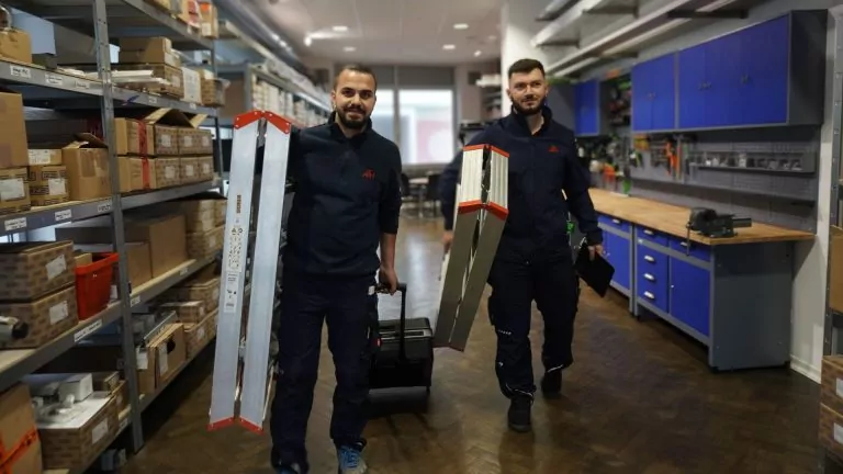 Zwei ATH-Mitarbeiter tragen Leitern und Werkzeug durch die Werkstatt.